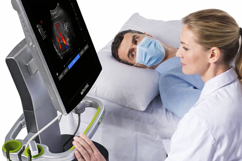 A healthcare professional using the Navi ultrasound system to examine a patient lying on a bed, with the screen displaying a colorful tissue scan of the patient’s body.