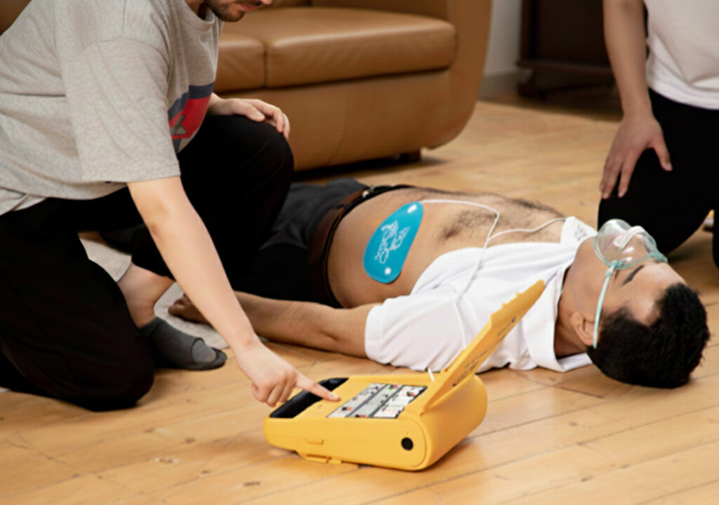 Operating the Amoul Semi-Automatic External Defibrillator on a patient lying down, with the defibrillator pads placed on the patient's body for emergency defibrillation.